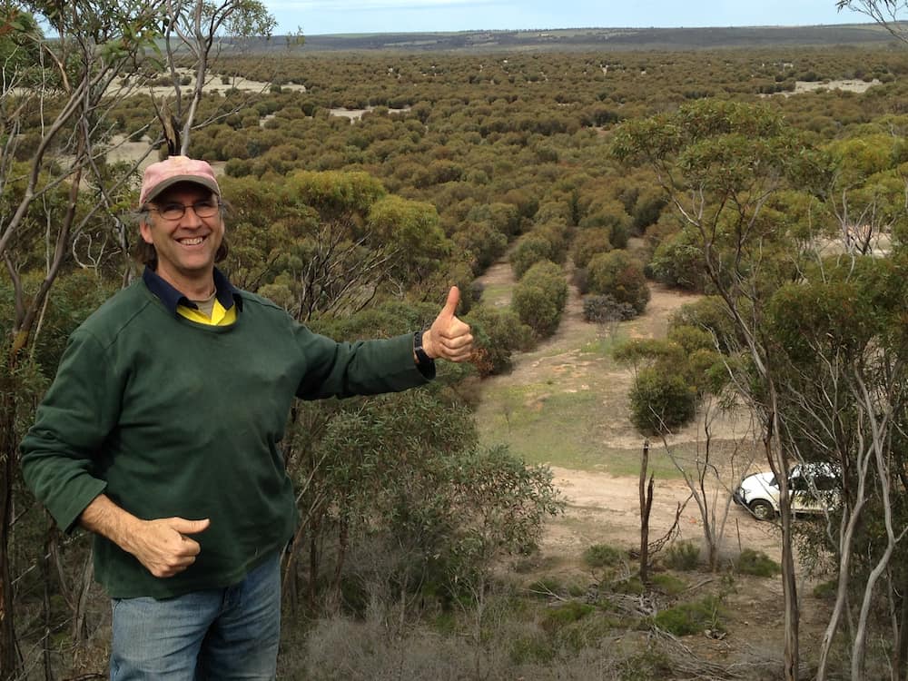 A man stands in front of a wide expanse of revegetation with his thumb up.